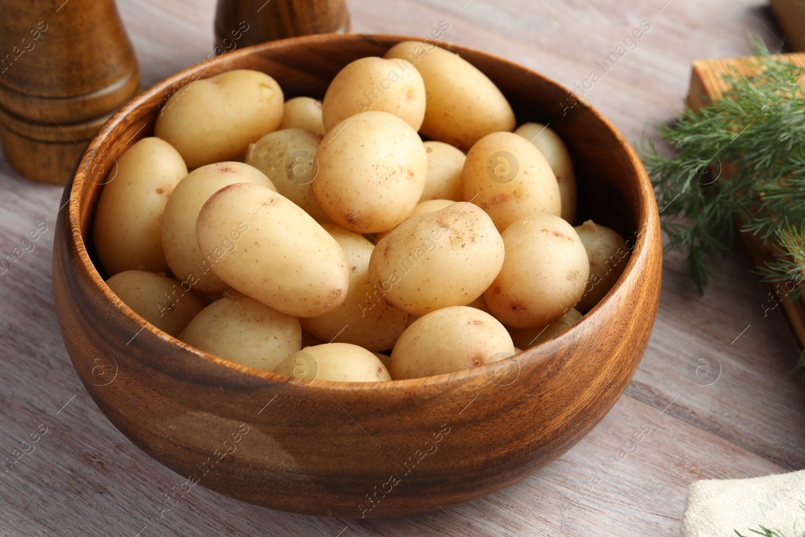 Photo of Boiled potatoes in bowl and dill on wooden table