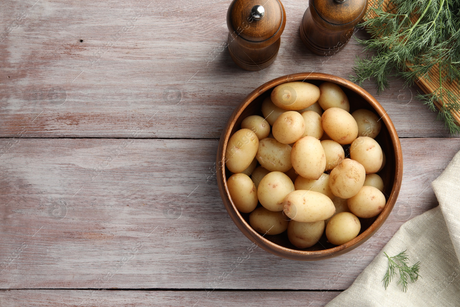 Photo of Boiled potatoes in bowl and dill on wooden table, top view. Space for text