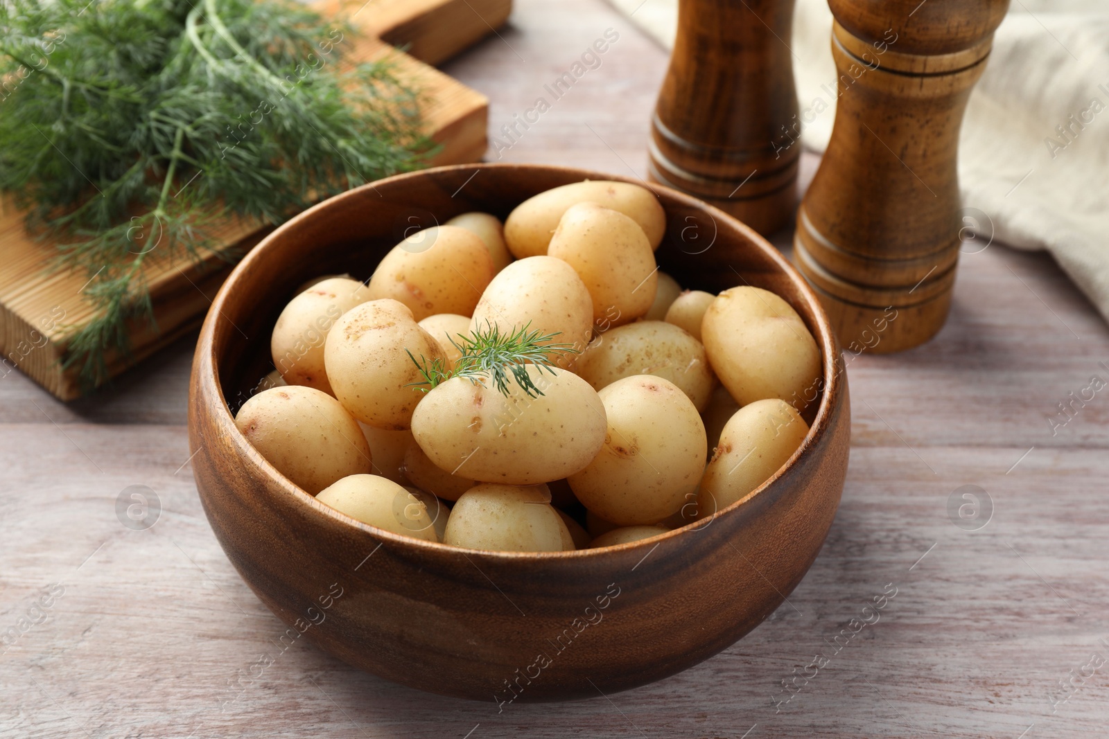 Photo of Boiled potatoes in bowl and dill on wooden table