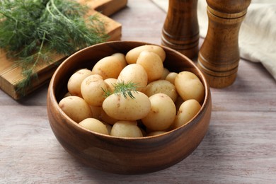 Boiled potatoes in bowl and dill on wooden table