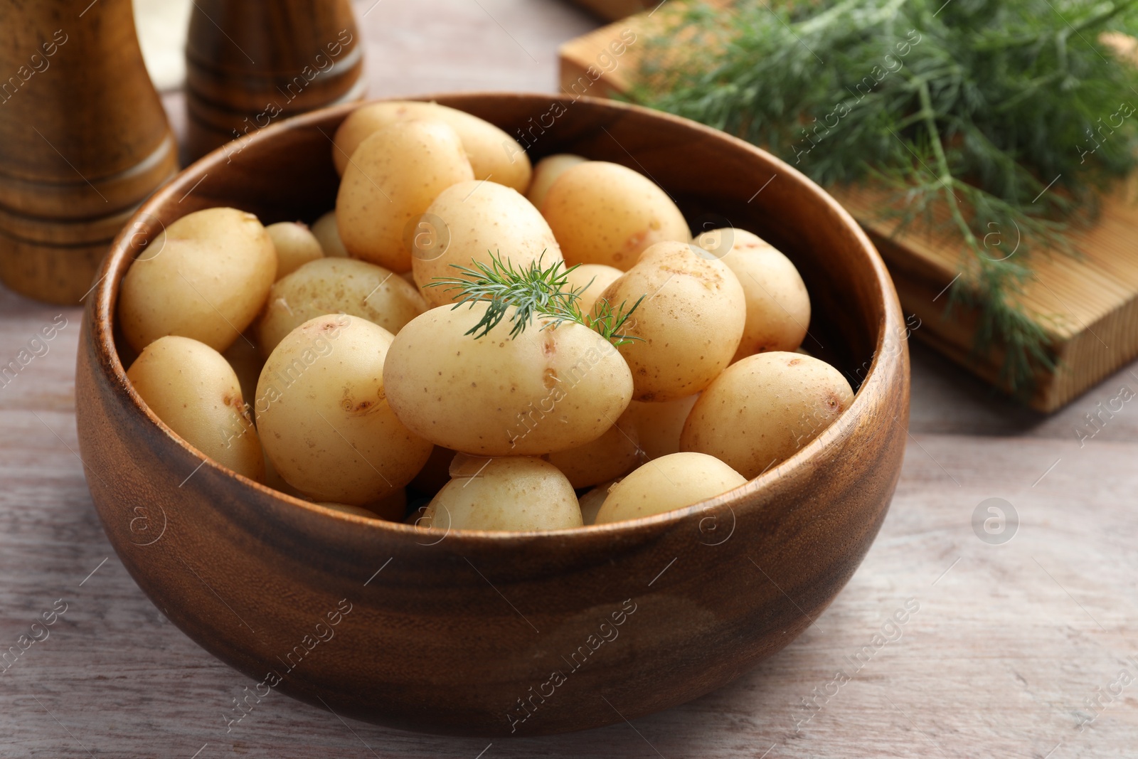 Photo of Boiled potatoes in bowl and dill on wooden table, closeup