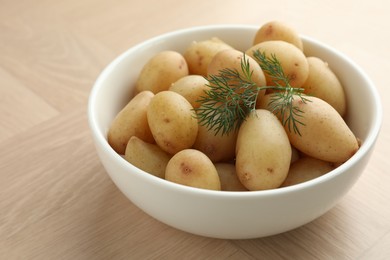 Boiled potatoes with dill in bowl on wooden table, closeup