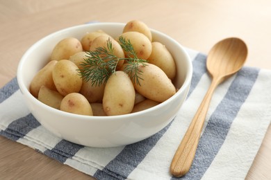 Photo of Boiled potatoes with dill in bowl and wooden spoon on table