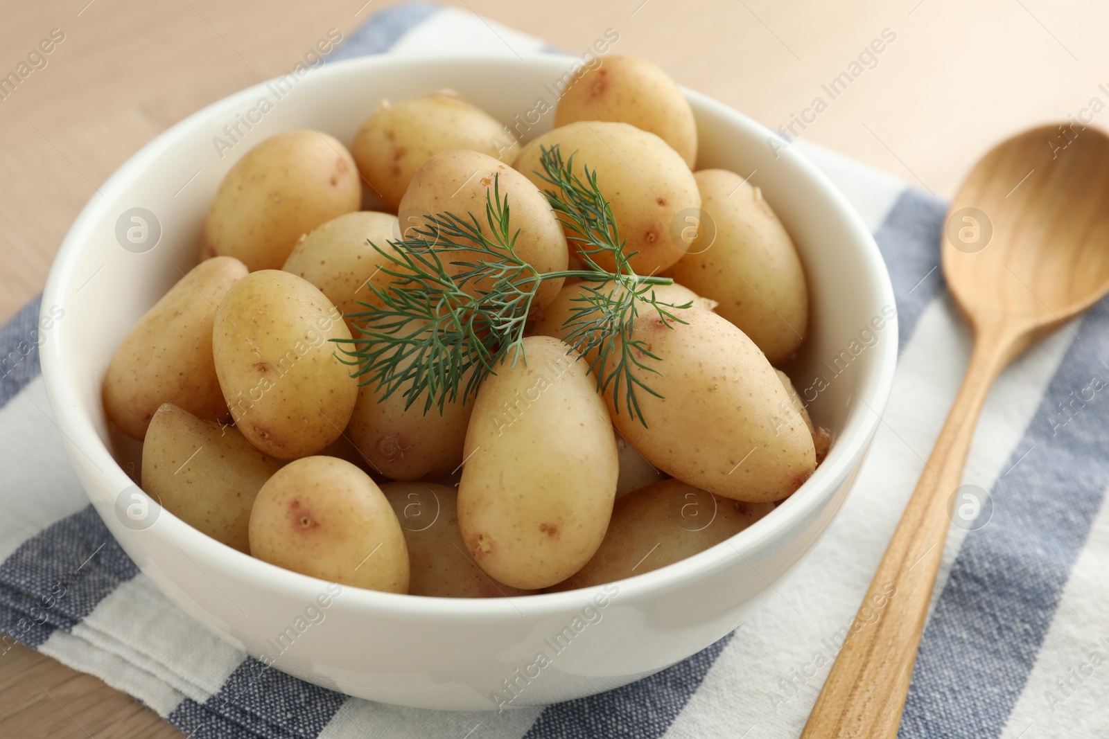 Photo of Boiled potatoes with dill in bowl and wooden spoon on table