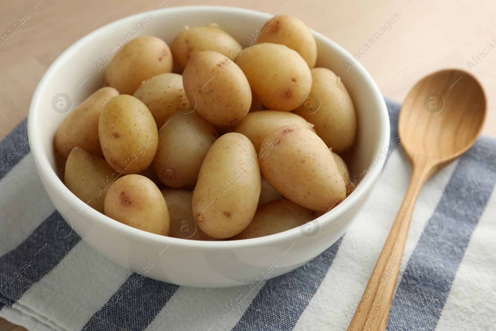 Photo of Boiled potatoes in bowl and wooden spoon on table