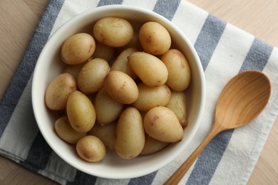 Boiled potatoes in bowl and wooden spoon on table, top view