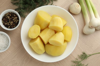 Photo of Boiled potatoes in bowl, spices, green onion and dill on wooden table, top view