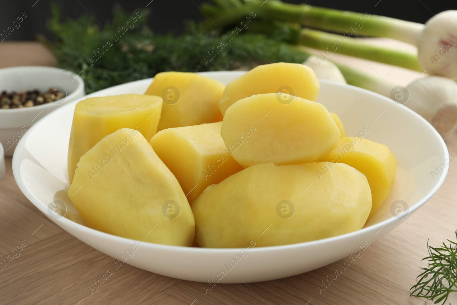 Photo of Boiled potatoes in bowl, dill and green onion on wooden table, closeup