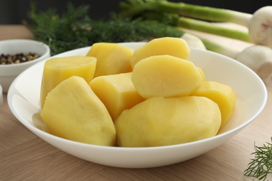 Boiled potatoes in bowl, dill and green onion on wooden table, closeup