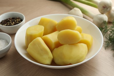 Boiled potatoes in bowl, spices, green onion and dill on wooden table