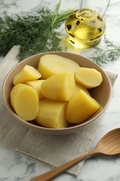 Boiled potatoes in bowl, dill, oil and spoon on white marble table