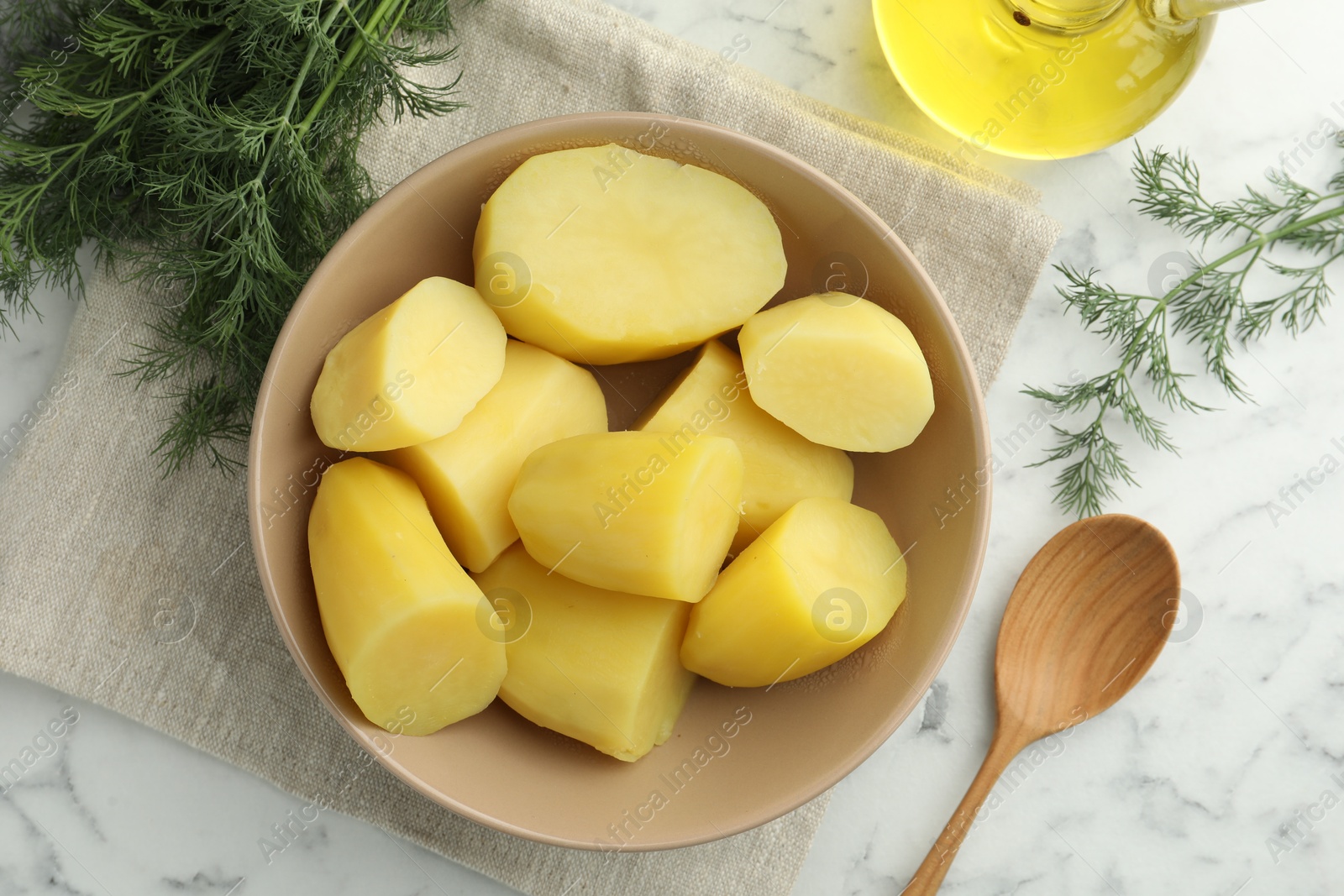 Photo of Boiled potatoes in bowl, dill, oil and spoon on white marble table, top view