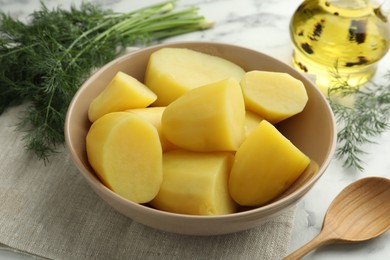 Photo of Boiled potatoes in bowl, dill, oil and spoon on white marble table