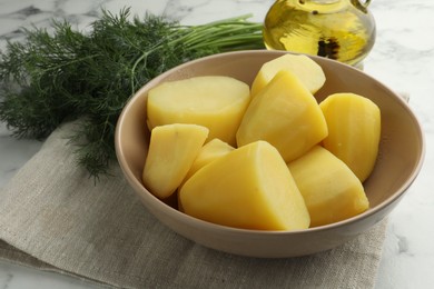 Boiled potatoes in bowl, dill and oil on white marble table