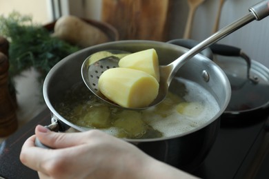 Photo of Woman taking boiled potato from pot on stove, closeup