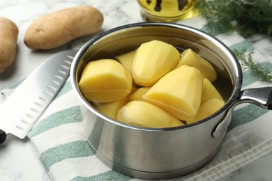 Raw potatoes in saucepan and knife on table