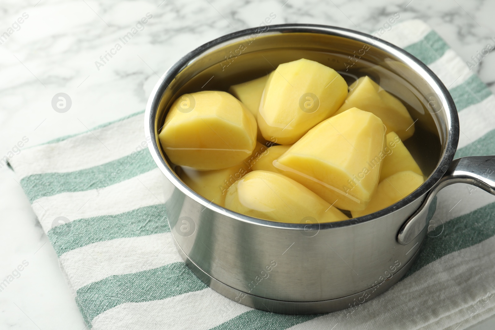 Photo of Raw potatoes in saucepan on white marble table