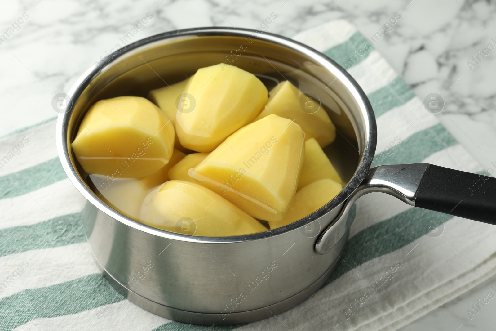 Photo of Raw potatoes in saucepan on white marble table