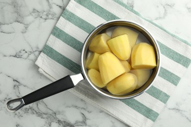 Raw potatoes in saucepan on white marble table, top view