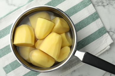 Raw potatoes in saucepan on white marble table, top view