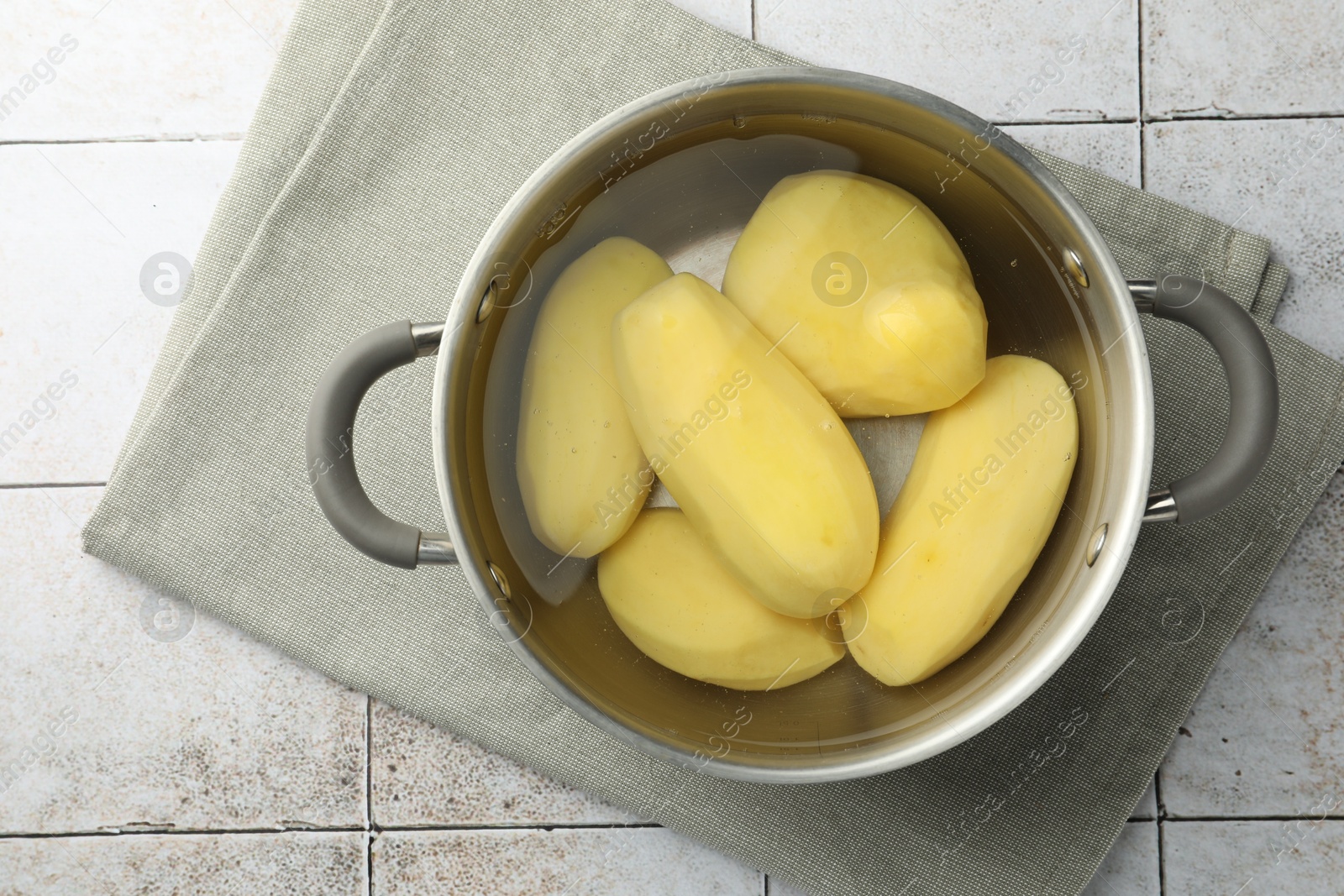 Photo of Raw potatoes in pot with water on tiled table, top view