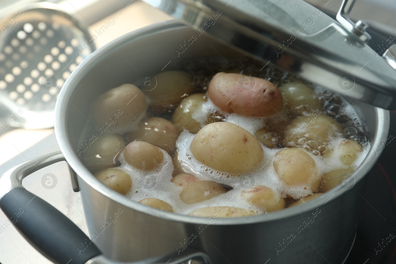 Photo of Boiling potatoes in pot on stove in kitchen, closeup