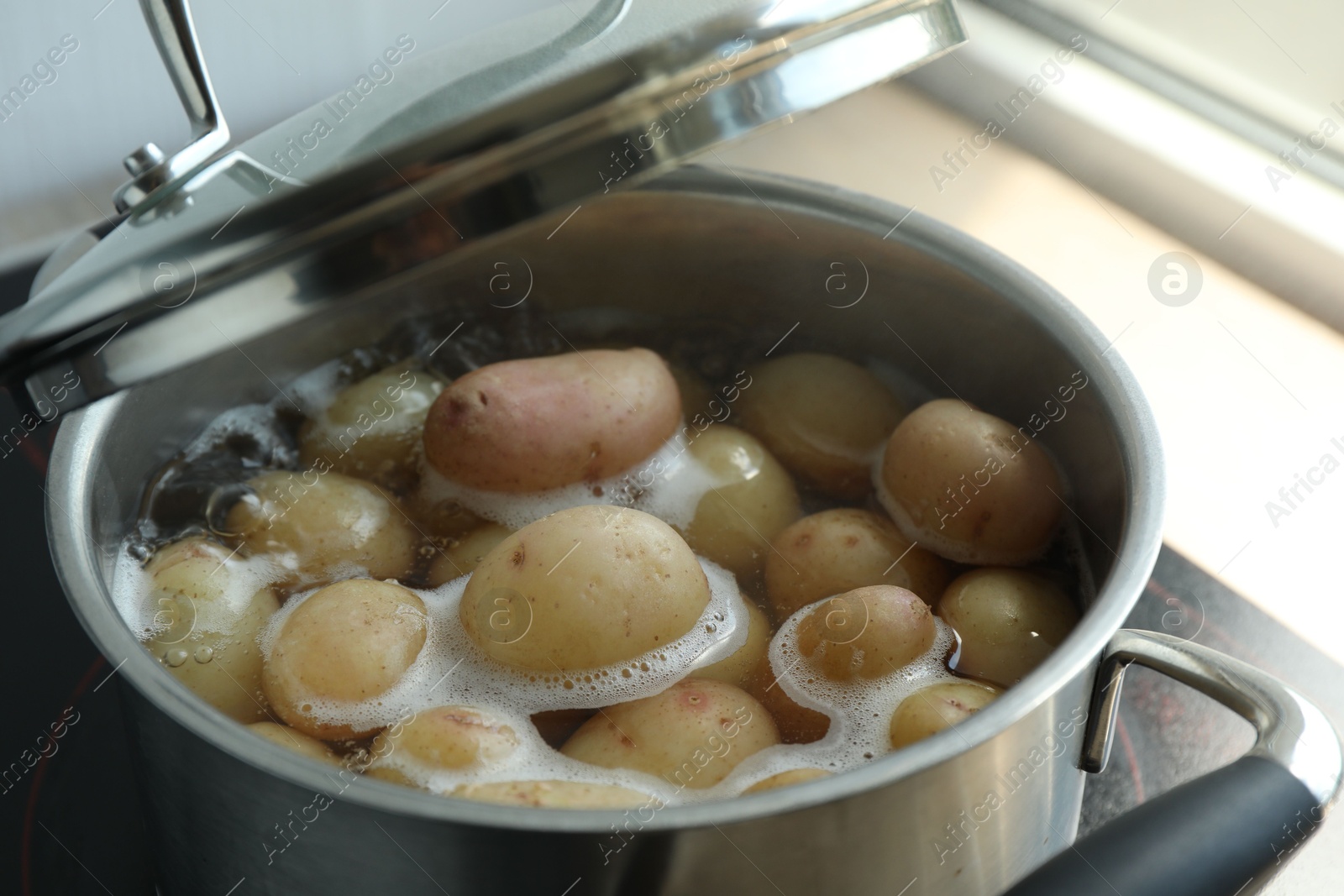 Photo of Boiling potatoes in pot on stove in kitchen, closeup