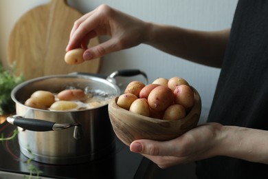 Woman putting potato into pot on stove, closeup