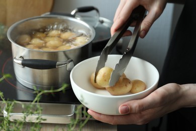 Woman taking potato from bowl at table, closeup