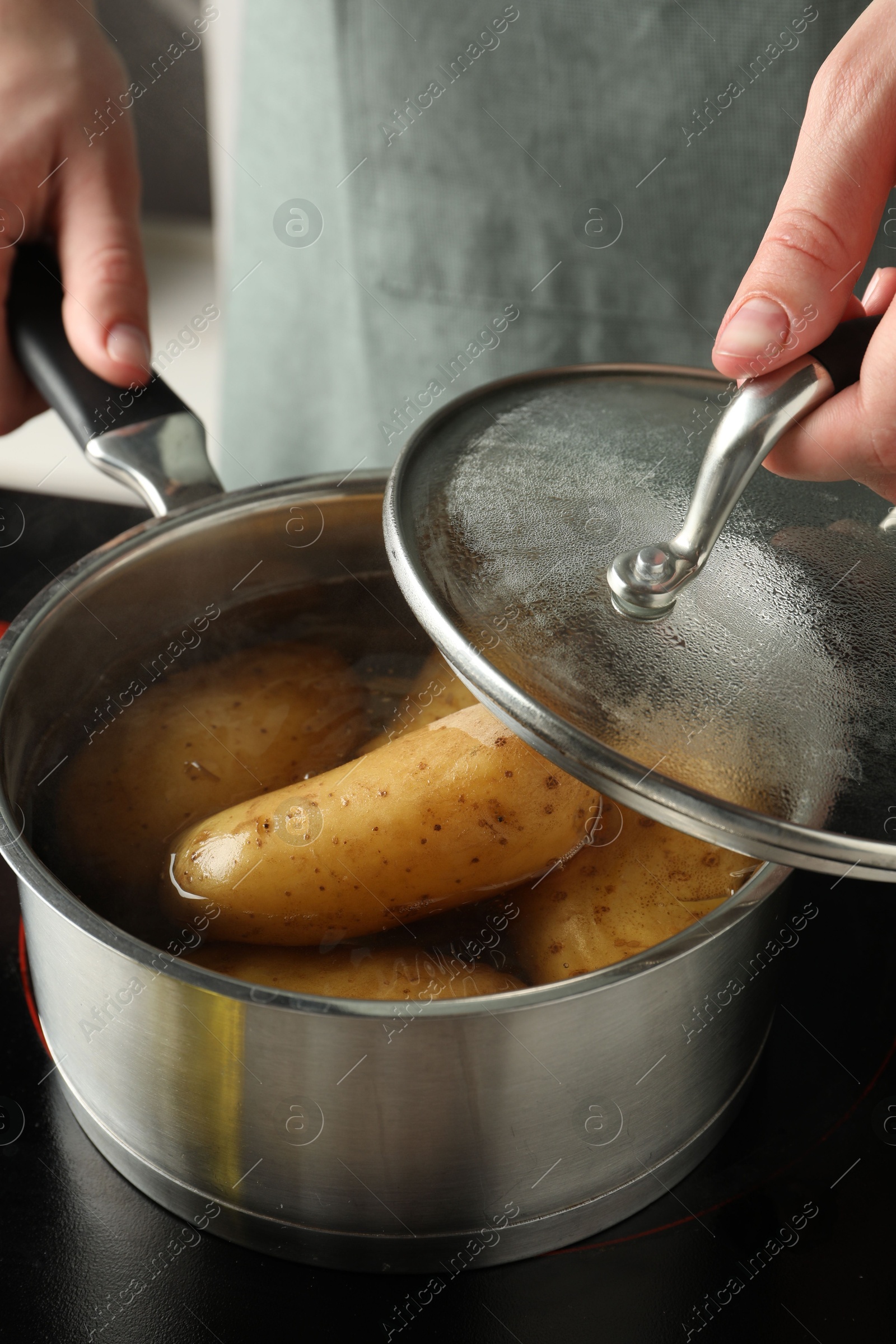 Photo of Woman boiling potatoes in saucepan on stove, closeup