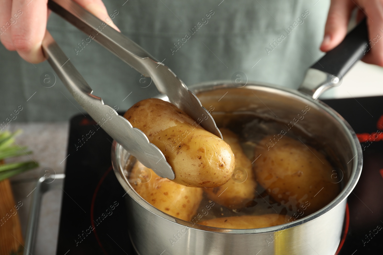 Photo of Woman taking boiled potato from saucepan on stove, closeup