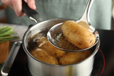 Photo of Woman taking boiled potato from saucepan on stove, closeup