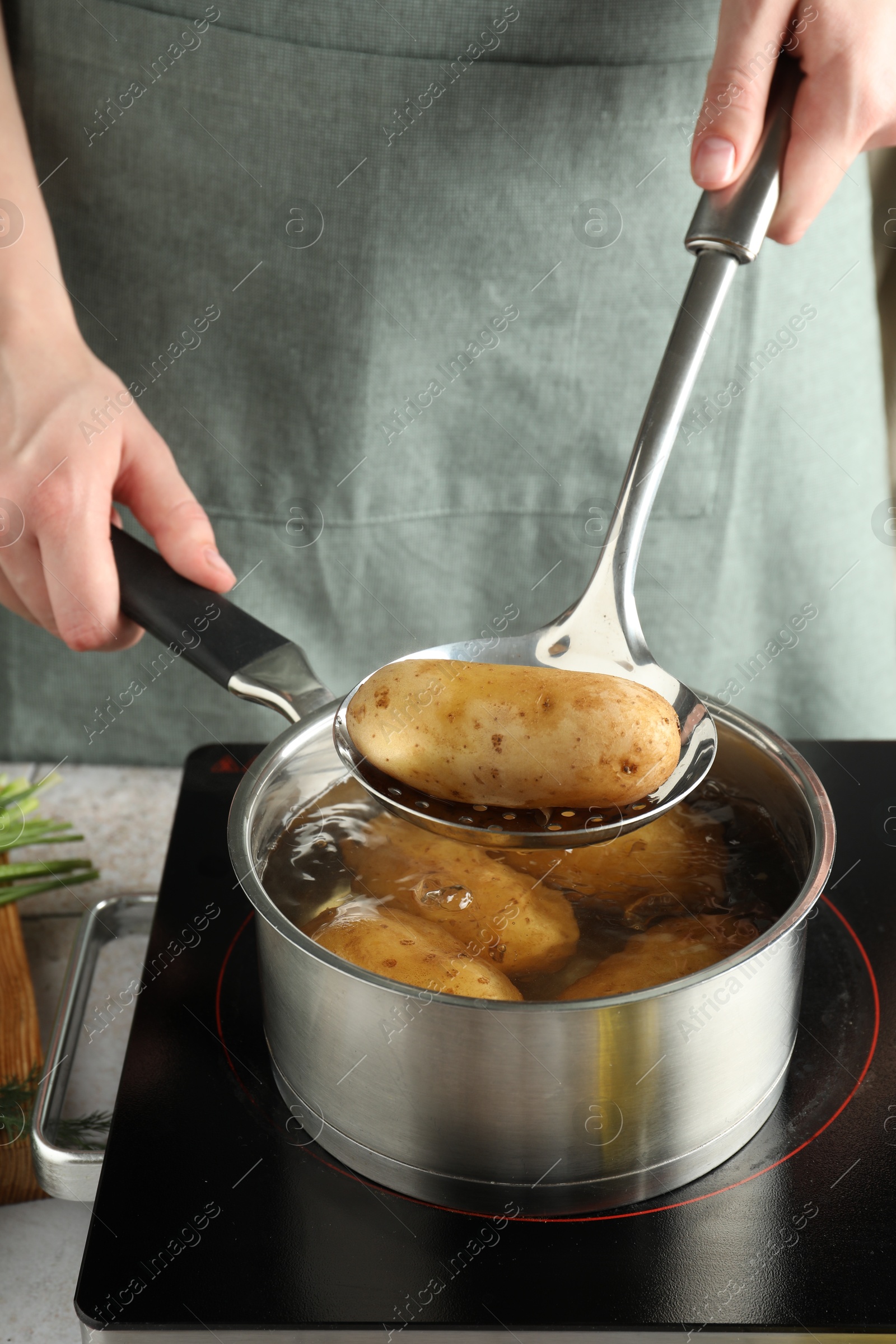 Photo of Woman taking boiled potato from saucepan on stove, closeup