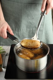 Photo of Woman taking boiled potato from saucepan on stove, closeup