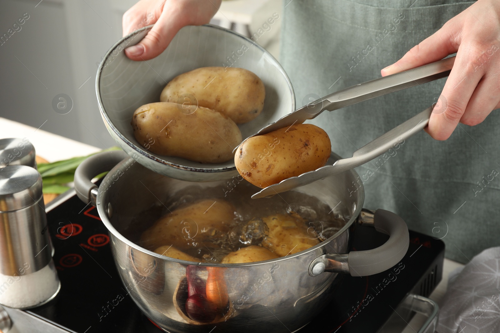 Photo of Woman putting raw potato into pot on stove, closeup