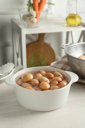 Raw potatoes in pot with water on white wooden table in kitchen