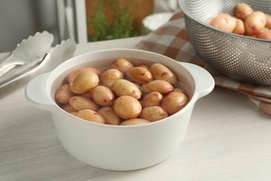 Raw potatoes in pot with water on white wooden table in kitchen