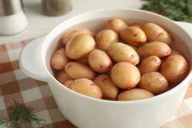 Raw potatoes in pot with water and dill on table, closeup