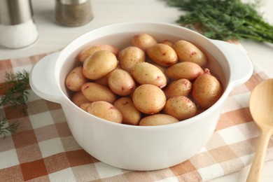 Raw potatoes in pot with water, dill and spoon on table