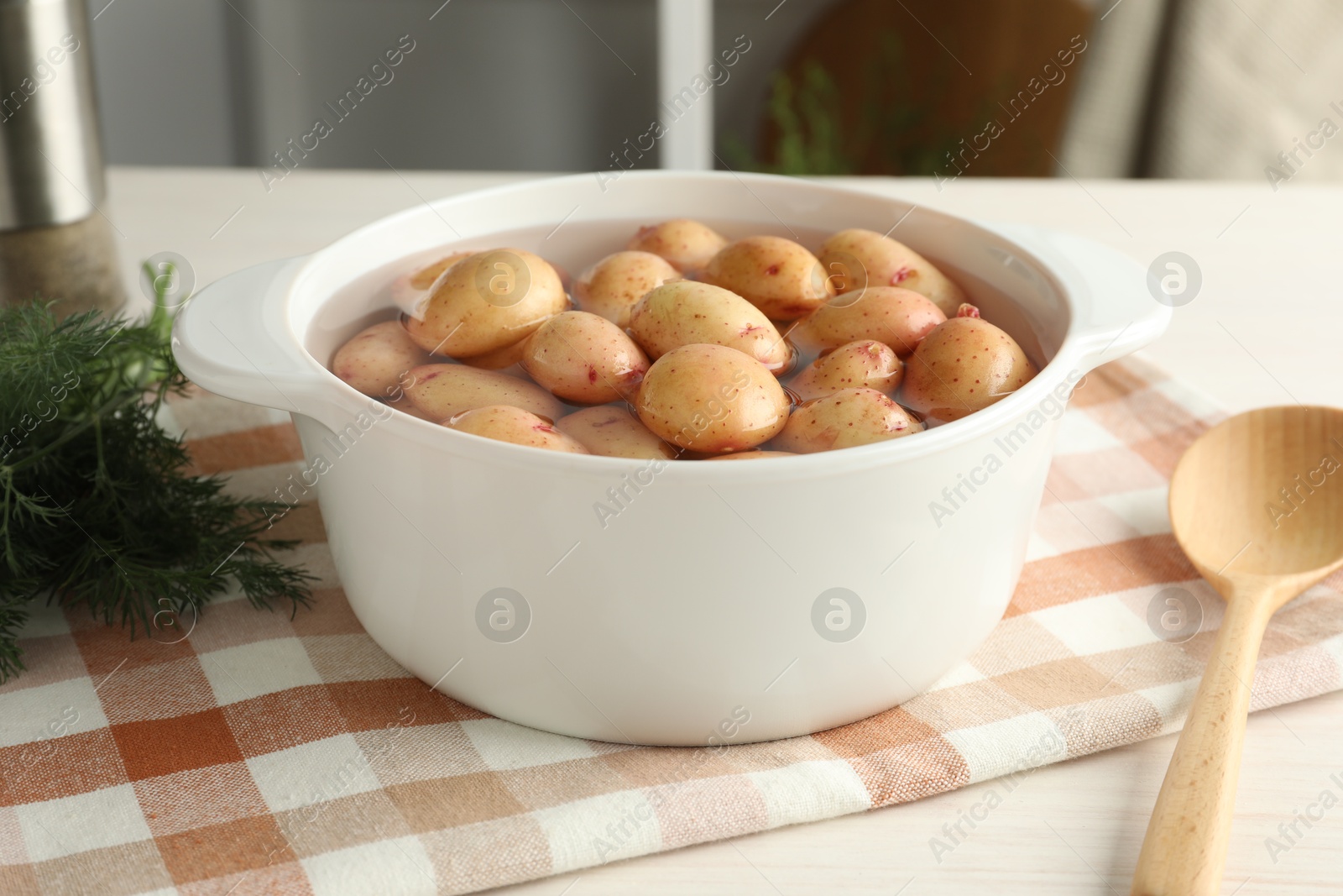 Photo of Raw potatoes in pot with water, dill and spoon on table