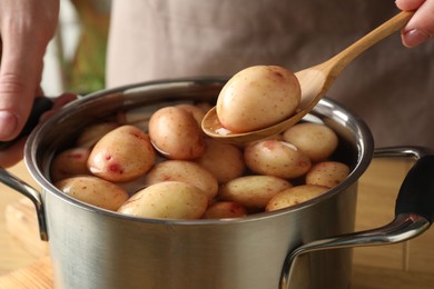 Woman putting raw potato into pot at table, closeup