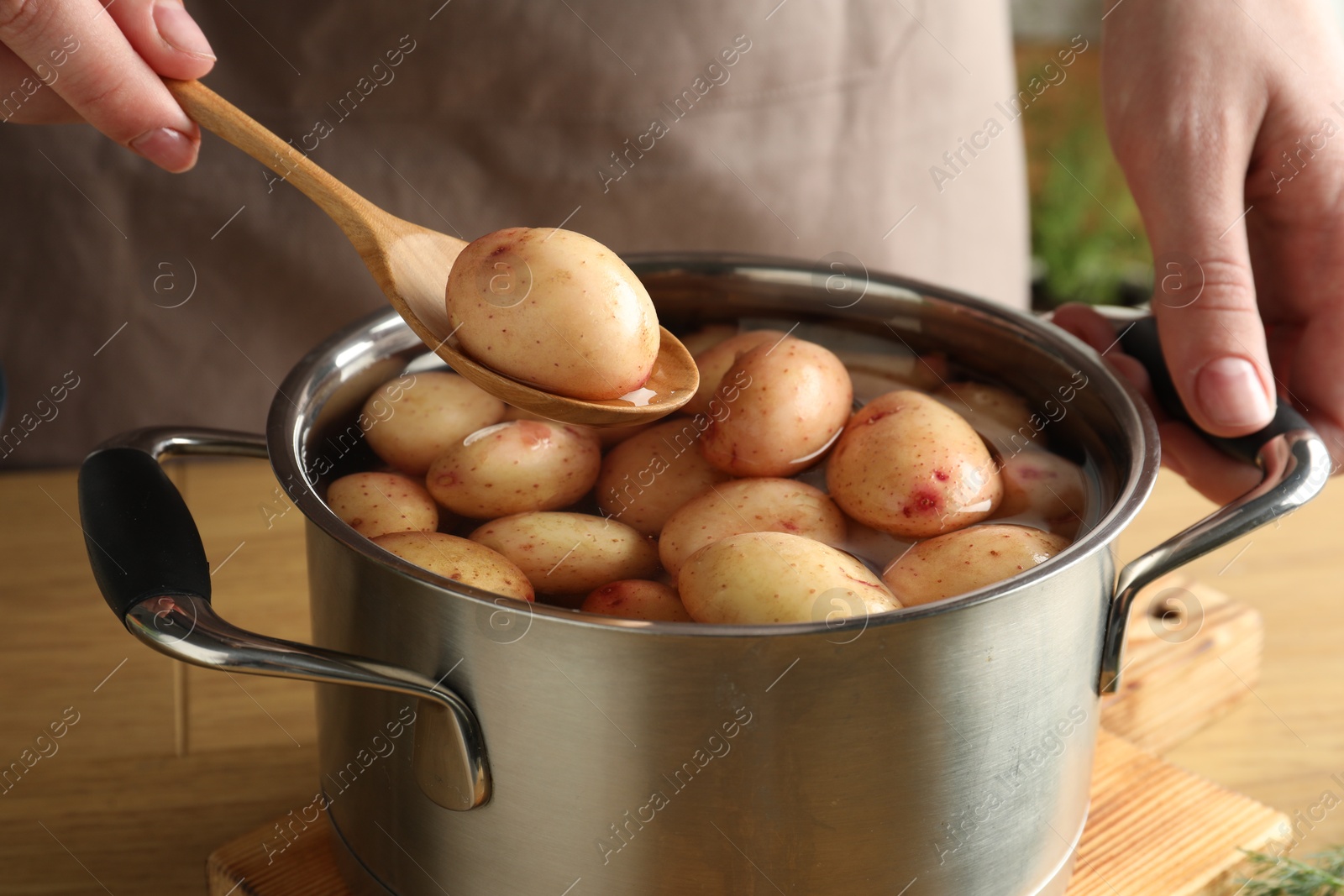 Photo of Woman putting raw potato into pot at wooden table, closeup