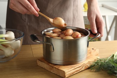 Woman putting raw potato into pot at wooden table, closeup