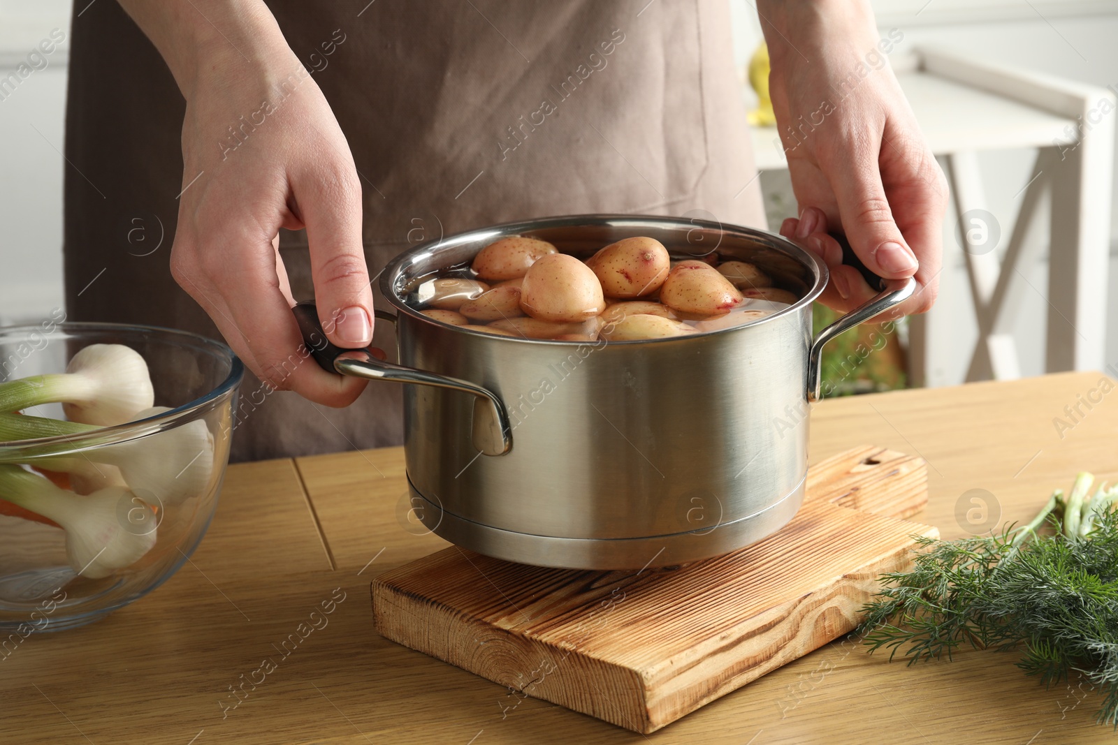 Photo of Woman holding pot with raw potatoes at wooden table, closeup