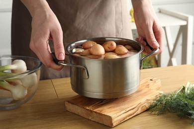 Photo of Woman holding pot with raw potatoes at wooden table, closeup