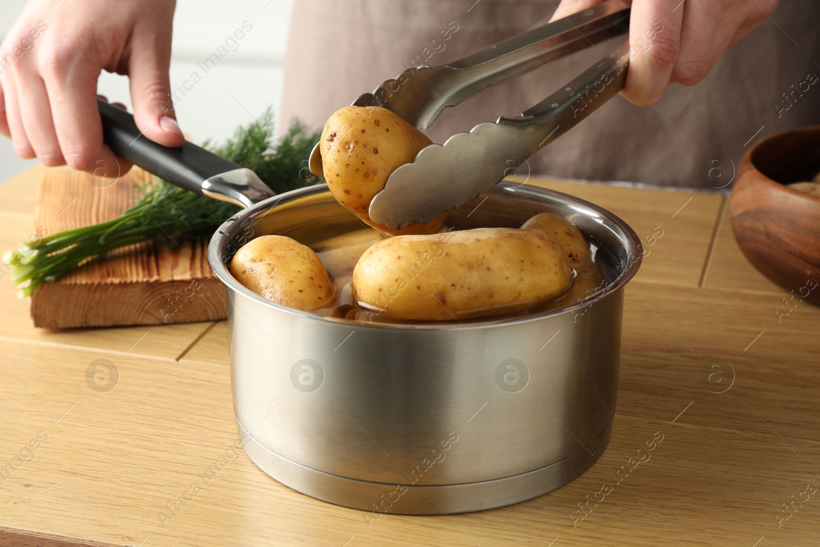 Photo of Woman putting raw potato into saucepan at wooden table, closeup