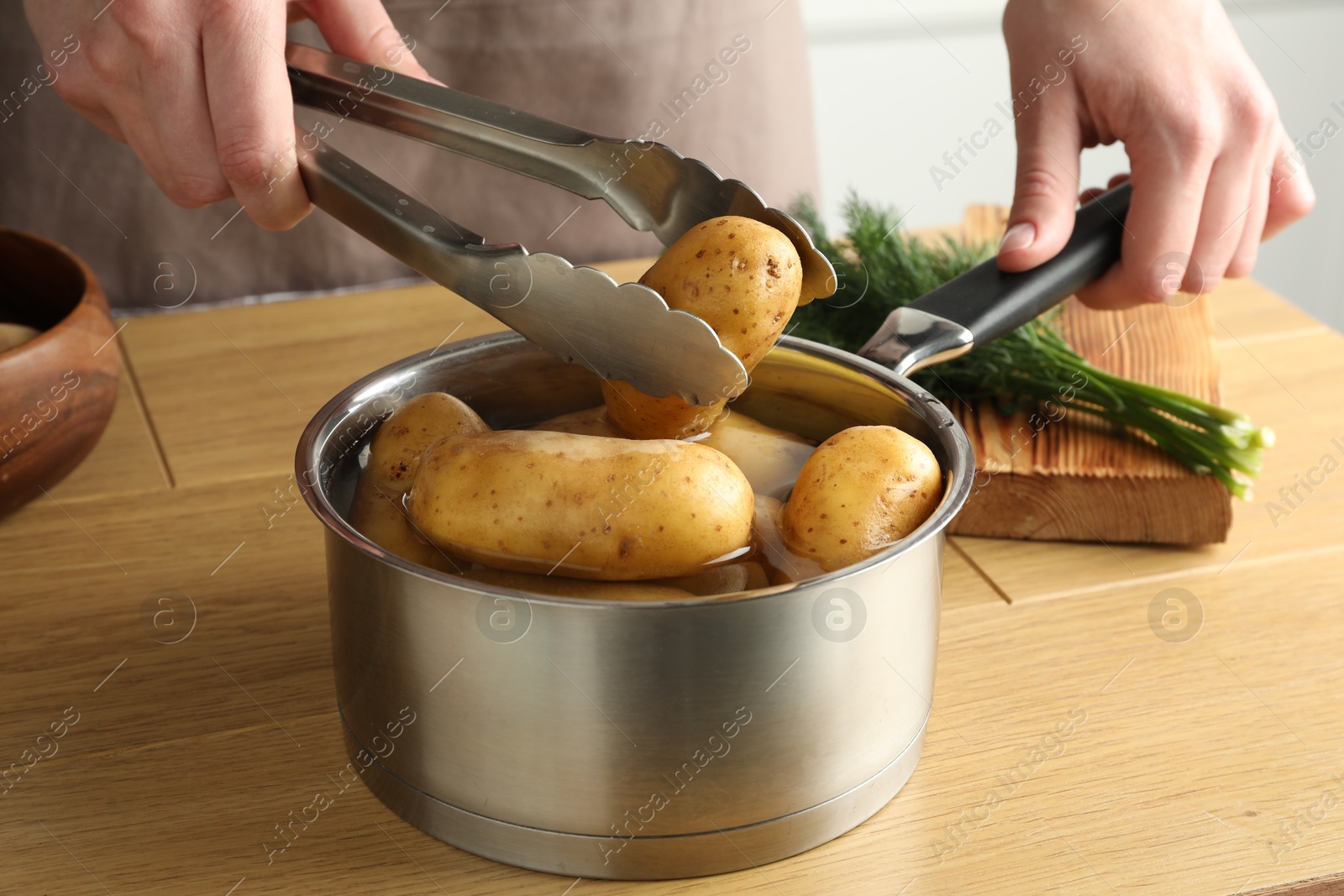 Photo of Woman putting raw potato into saucepan at wooden table, closeup