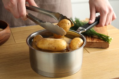 Woman putting raw potato into saucepan at wooden table, closeup