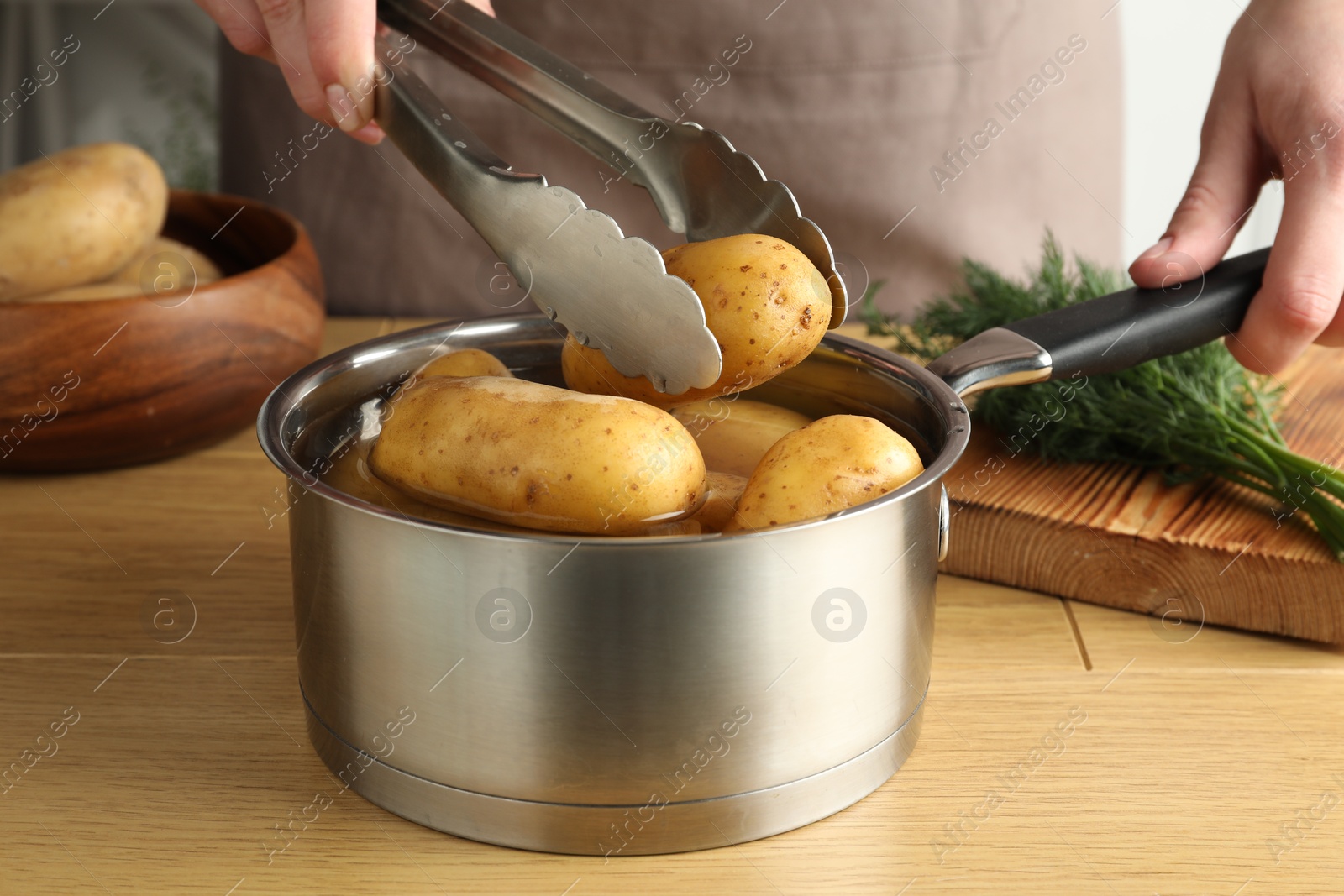 Photo of Woman putting raw potato into saucepan at wooden table, closeup