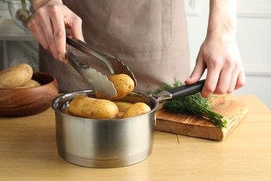 Woman putting raw potato into saucepan at wooden table, closeup